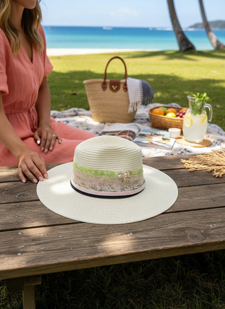 Adams + Hegwood off-white straw fedora with a layered ribbon, lace, and pearl bow band on a wooden picnic table.