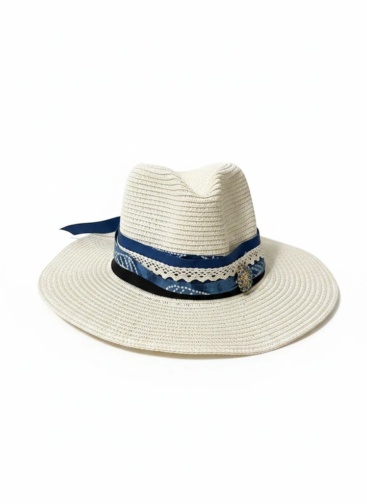 Adams + Hegwood woven straw fedora with a blue patterned ribbon, lace trim, and decorative brooch on a white background