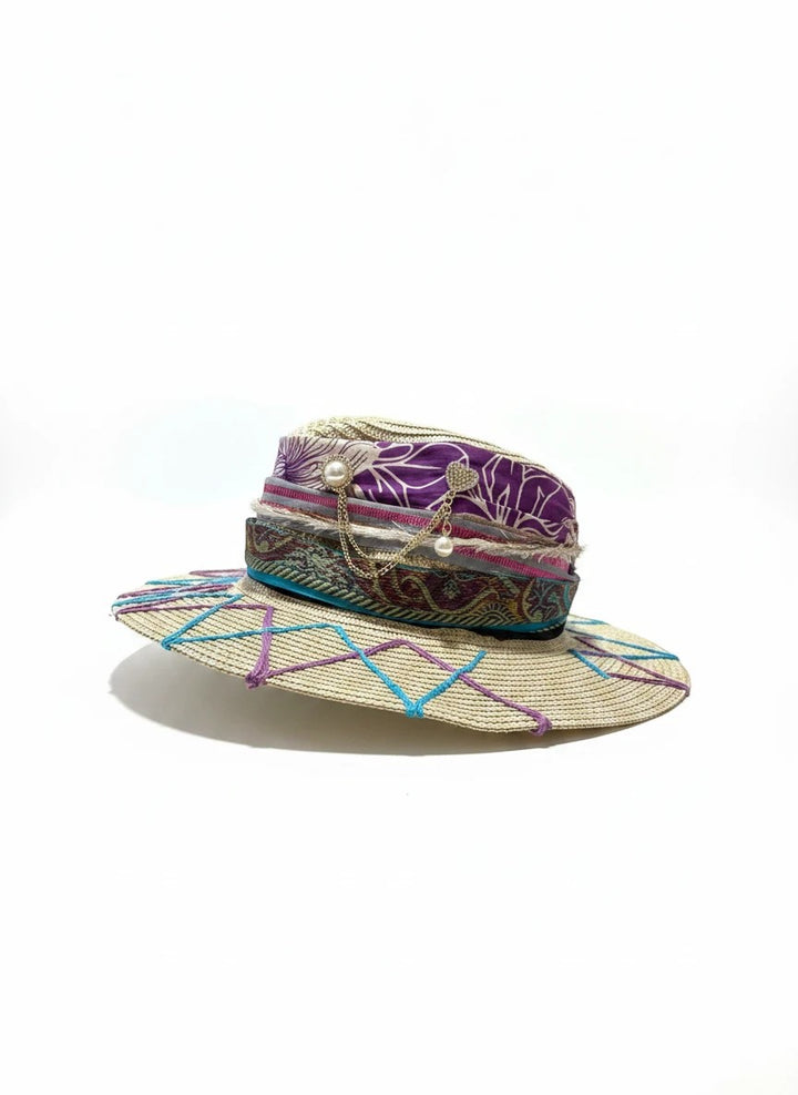 Adams + Hegwood decorative woven straw sun hat with purple floral ribbon, pearl and gold heart charms, and blue/purple stitching.