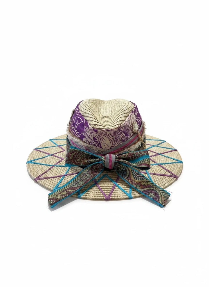 Adams + Hegwood decorative woven straw sun hat with purple floral ribbon, teal ribbon bow, pearl charms, and geometric stitching.