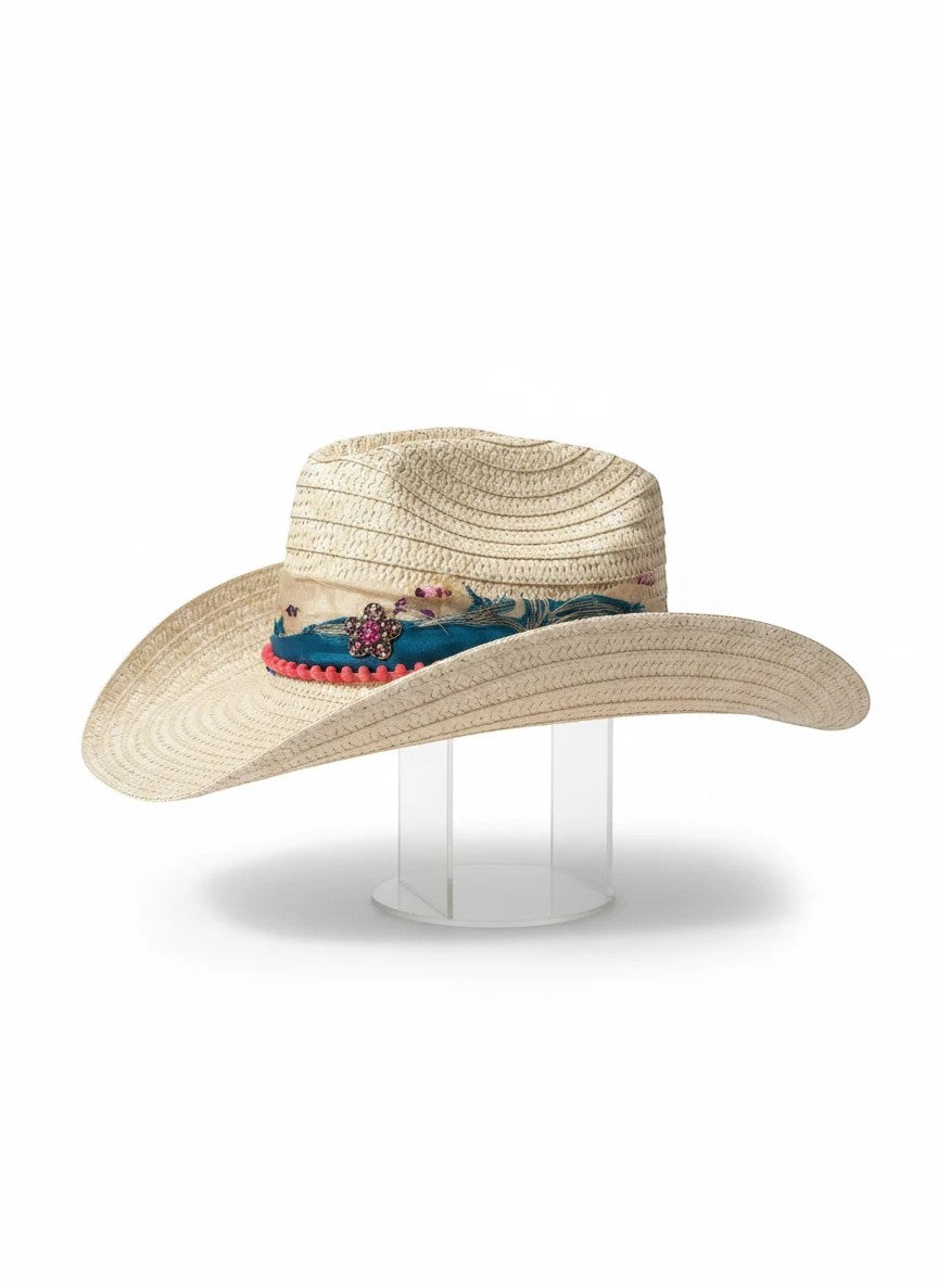 Adams + Hegwood woven straw Western hat with blue fabric band, pink pom-poms, and floral embellishment.