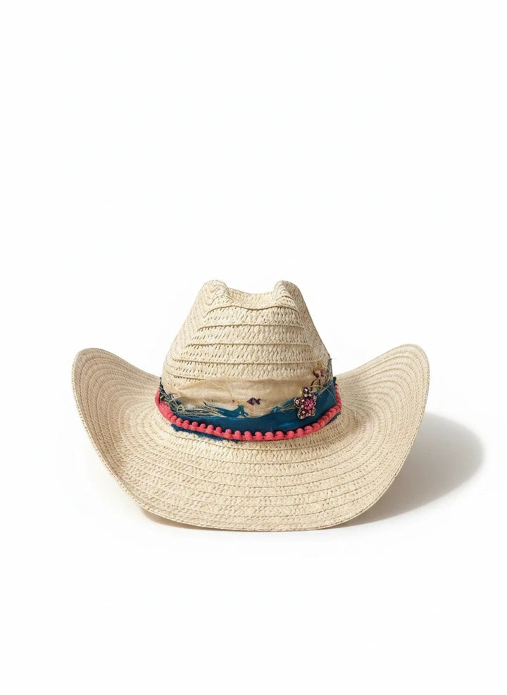 Adams + Hegwood woven straw Western hat with a blue patterned band, pink pom-pom trim, and floral embellishment.