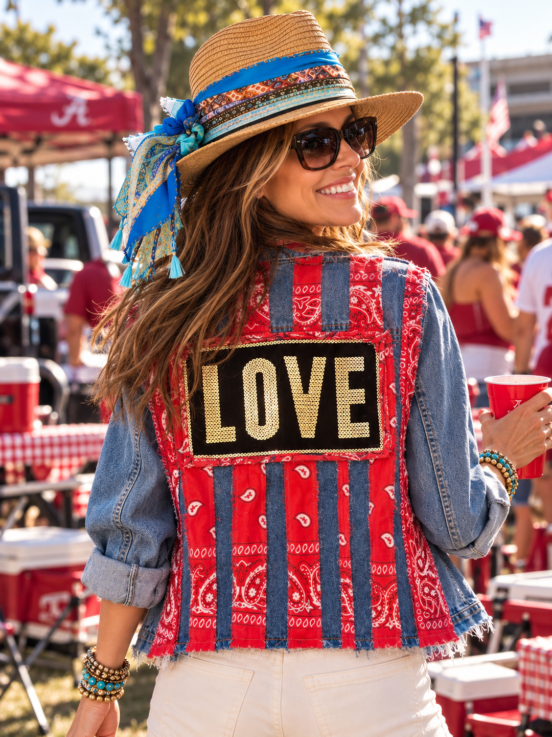 Woman at a tailgate wearing The Denim Muse handmade denim jacket, back view showing red bandana stripes and a gold sequin LOVE patch