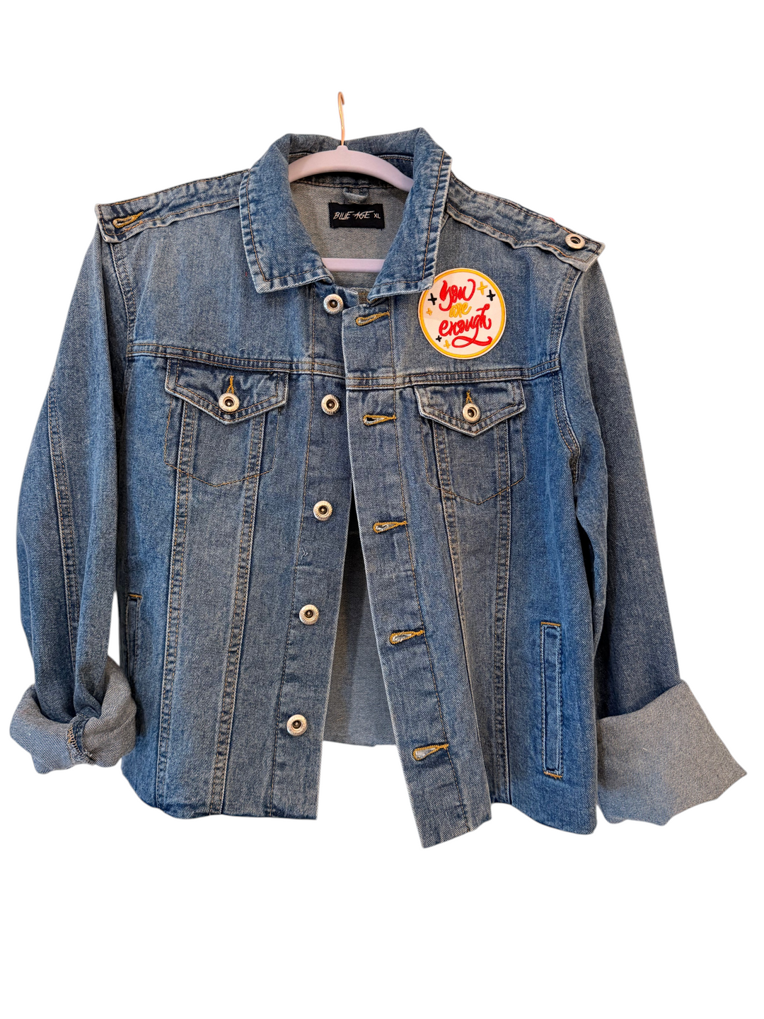 The Denim Muse handmade XL denim jacket on a hanger, front view with You Are Enough patch