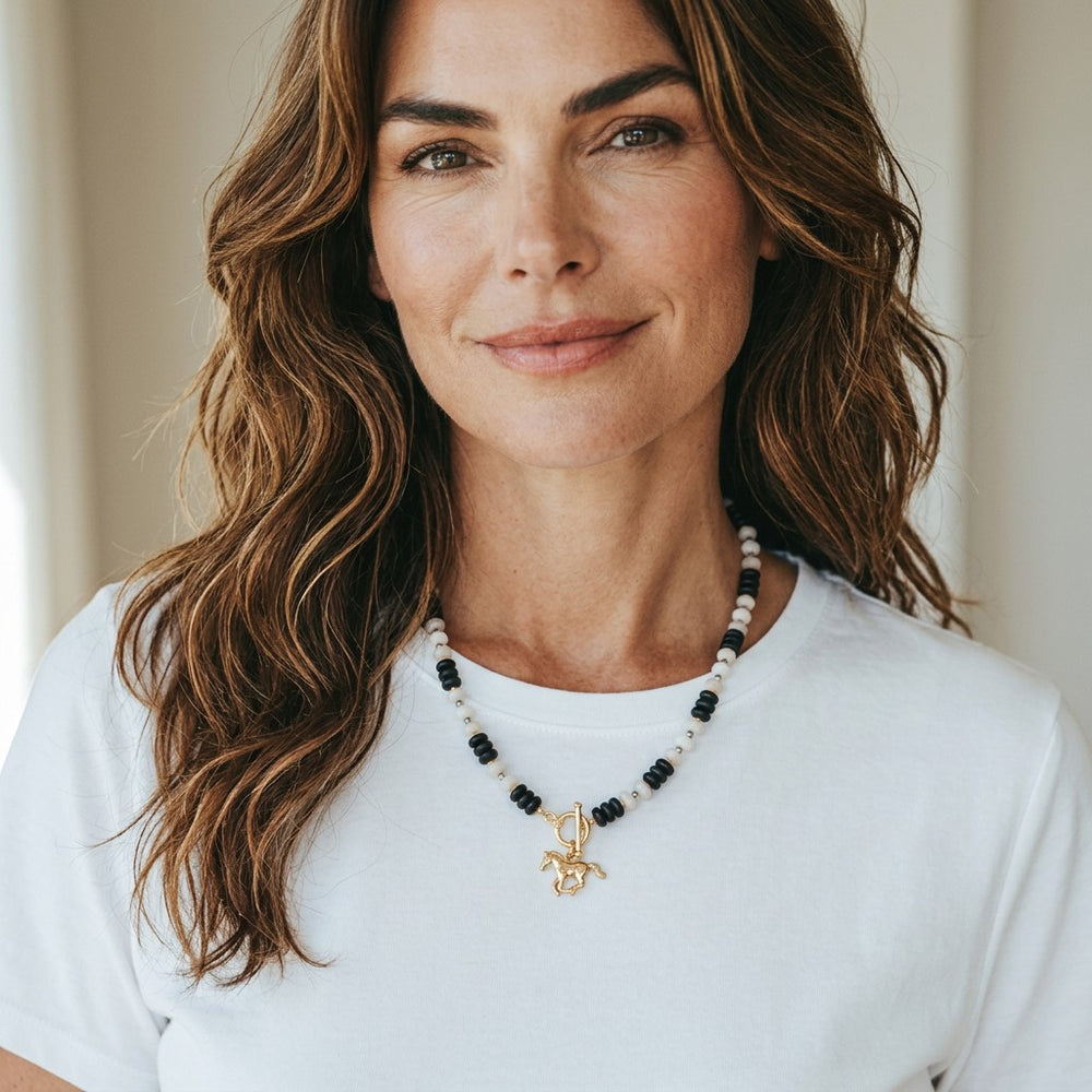 Woman wearing a Natalie Adams Hegwood Studio beaded necklace with a gold horse pendant and toggle clasp