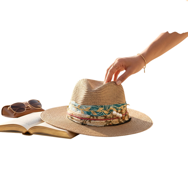Natalie Adams Hegwood Studio woven straw fedora with a multi-colored leaf print band and pearl accents on a table